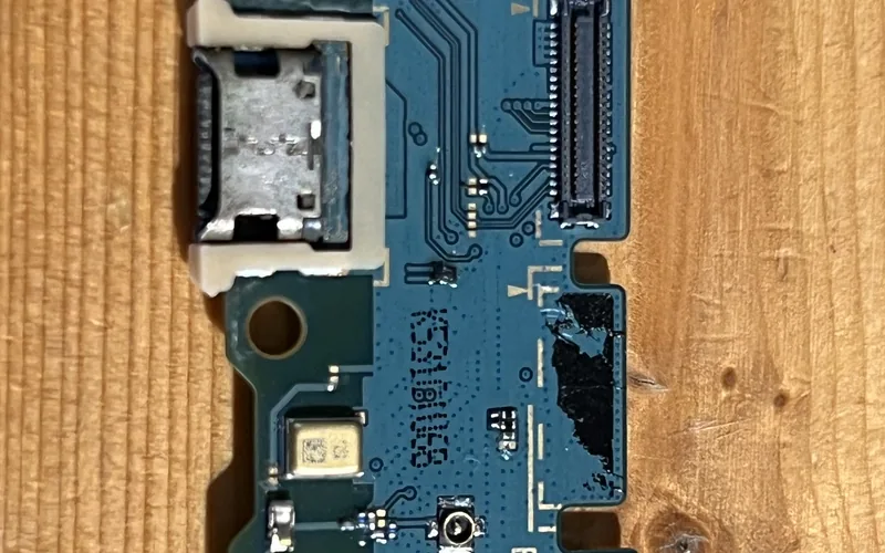 Samsung Galaxy A16 進水後拆下的充電尾插小板，板面可見不規則深色痕跡與連接埠內的腐蝕