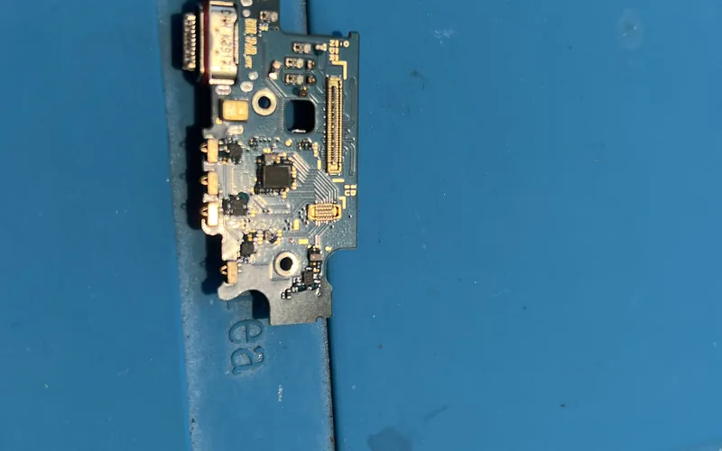 Samsung Galaxy S22+ 拆下的尾插小板放在藍色維修墊上，可見 USB-C 連接埠與板側的天線接點